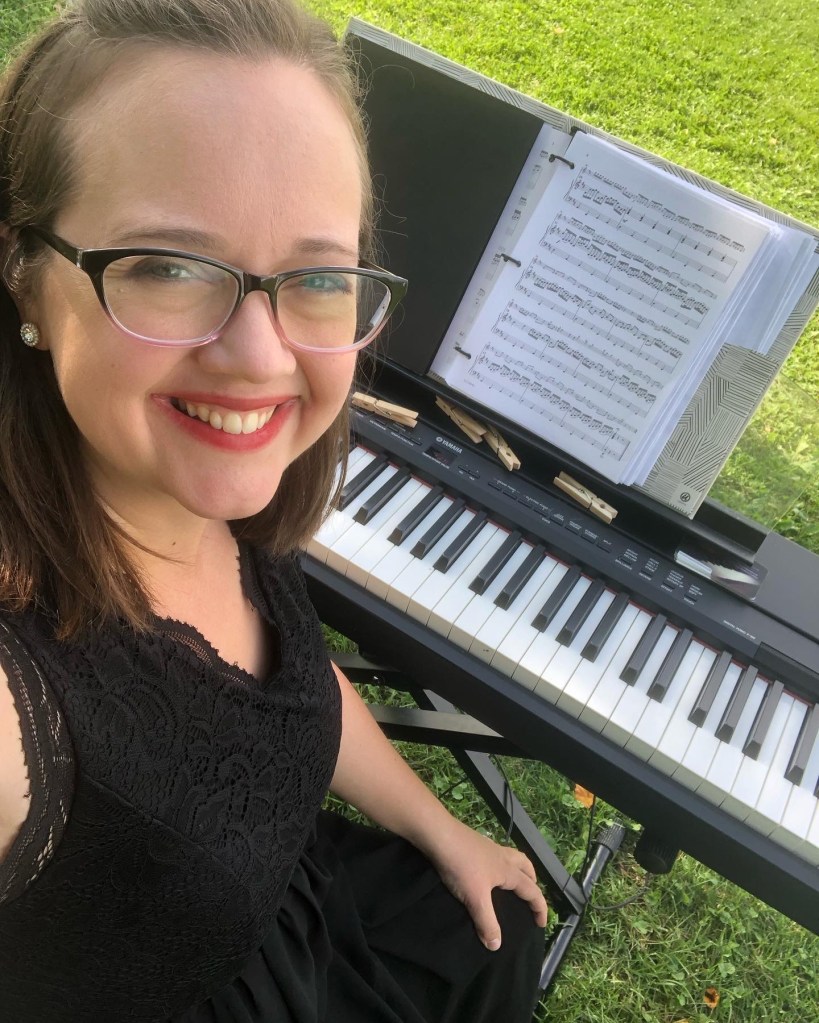 Piano Player for wedding Veronica Gomoll sits smiling in front of a digital piano with classical sheet music on the stand. The setting is a grassy field at an outdoor winery wedding in Maple Park, Illinois.